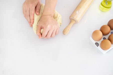 Top view of Hands kneading dough on white table, closeup, Flat lay. Woman kneading dough on table sprinkled with flour.Making bakery by female hands at home.の写真素材