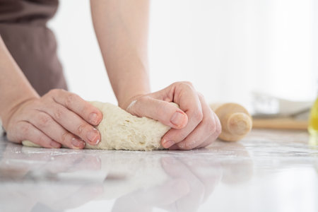 Woman kneading dough on table sprinkled with flour.Close up of  home baker chef is making with flour loaf of dough for preparation of pasta, pizza and other pastries in bright bakery kitchen.の写真素材