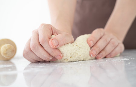 Close up of  home baker chef is making with flour loaf of dough for preparation of pasta, pizza and other pastries in bright bakery kitchen.Female hands making dough for pizza .の写真素材