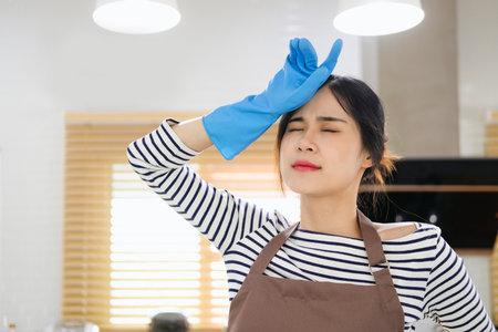 Exhausted millennial housewife in blue latex gloves wipe sweat from brow. Sad fatigued young woman too tired of household chores cleaning flat house dusting furnitureの写真素材