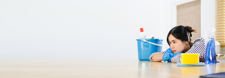 Tired young woman sitting in kitchen room with cleaning products and equipment, Housework conceptの写真素材