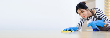Woman in protective gloves is smiling and wiping dust using a spray and a duster while cleaning her house, close-upの素材