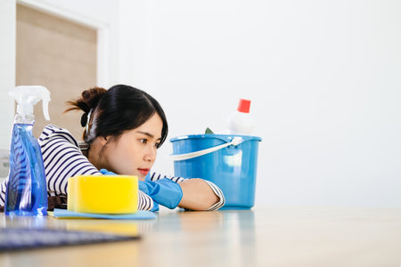 Frustrated Young Woman in apron and blue rubber gloves Sitting in Kitchen with  Cleaning Products At Home.の写真素材