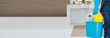 Unrecognizable millennial maid holding bucket with cleaning supplies indoors, closeup of hands. Cropped view of housewife with detergents, ready for house cleanup. Sanitary service conceptの写真素材