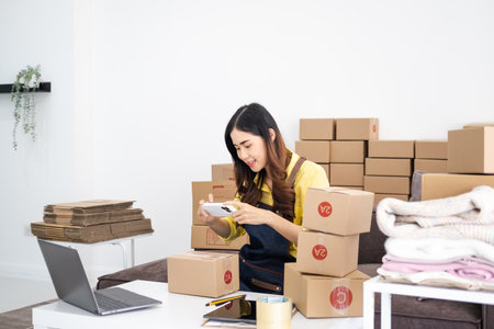 Small business owner packing in the cardbox at home office. Woman preparing a parcel for delivery at...