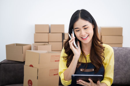 Startup small business SME, Entrepreneur owner talking on phone using tablet taking receive and checking online purchase shopping order to preparing pack product box. Selling online ideas conceptの写真素材