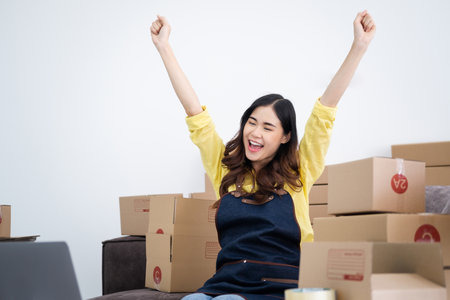 Happy young Asian woman entrepreneur, Smile for sales success after checking order from online shopping store in a laptop computer  at home office, Concept of merchant business online and eCommerceの写真素材