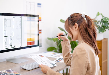 Thoughtful interior designer looking at computer screen while working at desk in office, Design develop for new interior project. Architecture renovation style design graphic.の写真素材