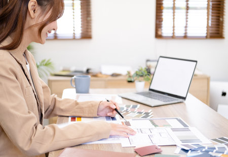 Professional interior designer working in the office, Portrait of young asian female architect working on business of Real estateproject , sketching on a house plan choosing swatches and material.の写真素材