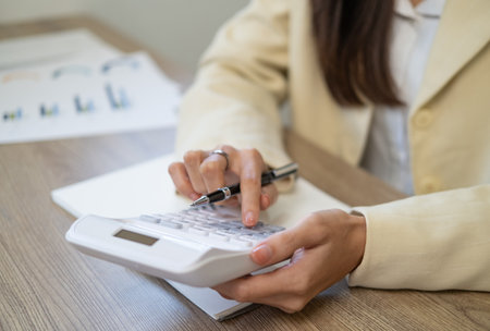 Close-up woman hand press calculator to calculate the company's financial results On the wooden table in the office and business work background, tax, accounting, statistics, and analytical research.の写真素材