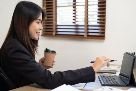 Woman working on laptop computer at workplace. Woman sitting at table with a coffee cup using a laptop at home office.の写真素材