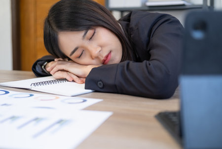 Overworked tired businesswoman sleeping on table in office. Young exhausted girl working from home. Woman using laptop. Entrepreneur, business, freelance work, student, stress, work from home conceptの写真素材