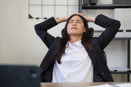 Stressed exhausted woman sitting at office desk and working overtime, she is overloaded with workの写真素材