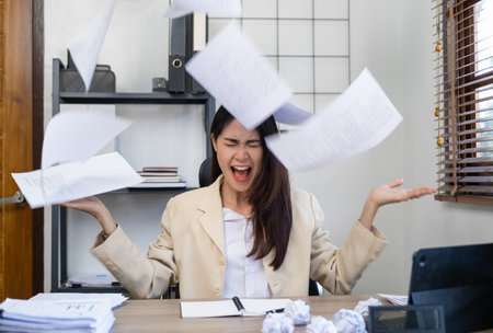 Stressed tired businesswoman feels exhausted sitting at office desk with laptop and crumpled paper,...