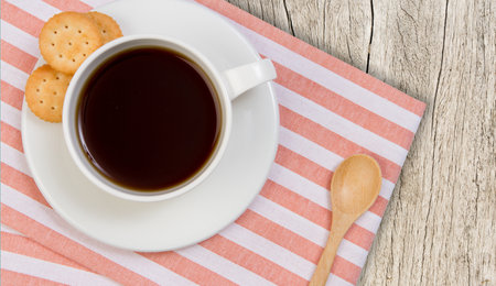 Top view of black coffee in white cup and biscuits on white and pink fabric striped table matの写真素材
