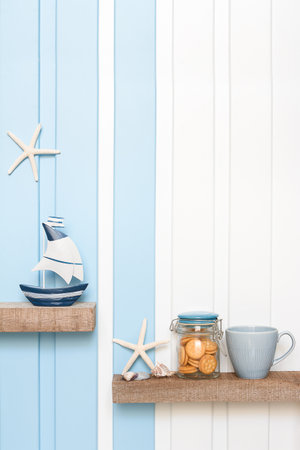 Summer sea decoration background - Front view of sailboat , starfish , seashell with coffee cup and cookie on shelf over blue white wall .の写真素材