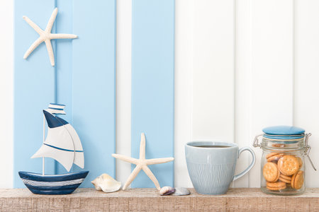 Summer sea decoration background - Front view of sailboat , starfish , seashell with coffee cup and cookie on shelf over blue white wall .の写真素材