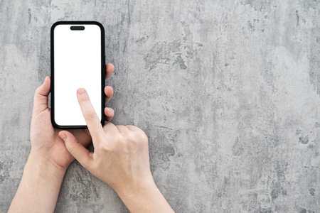 Woman hands holding mobile phone on polished concrete background with copy space. Flat lay. Top view.の写真素材