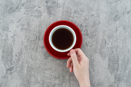 Young adult woman hands holding red cup of black coffee on polished concrete table background. Close...