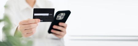 Close up female hands holding credit card and smartphone, young woman paying online, using banking...