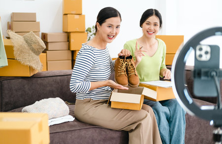 Young asian woman business owner at fashion store using smartphone live streaming for sale fashion clothing to customer and present detail on social media, Online shopping concept.の写真素材