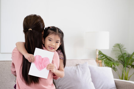 Happy mother's day! Child daughter congratulates mom and gives her card. Mum and girl smiling and hugging. Family holiday and togetherness.の写真素材