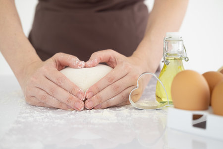 Baking with love on Valentine's Day. Cropped image of  woman cooking on kitchen making cakes and cookies. side view hands holding dough in heart shape.の写真素材