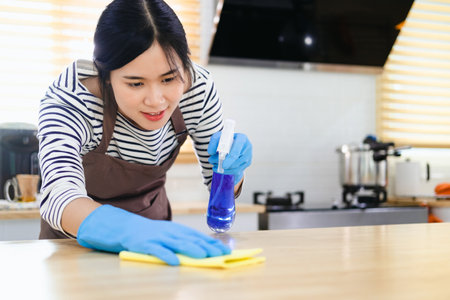 Asian housewife sanitizing surfaces cleaning home kitchen table with disinfectant spray bottle...