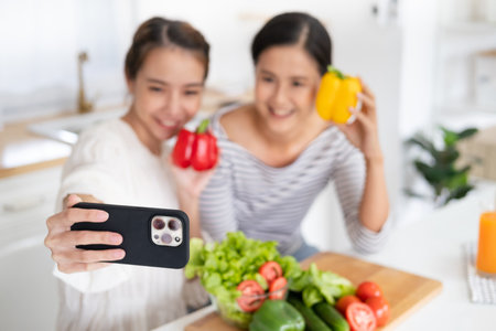 Asian woman girlfriends smiles, holds bell pepper and takes selfies in kitchenの写真素材
