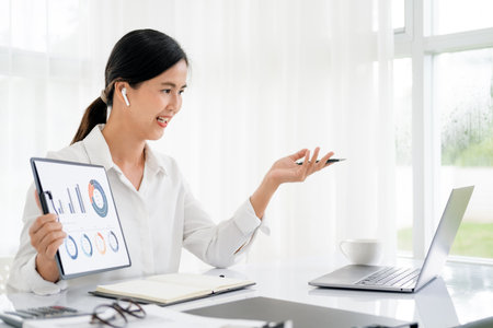 Asian business woman employee or executive manager using computer looking at laptop and talking leading hybrid conference remote video call virtual meeting or online training working in office.の写真素材