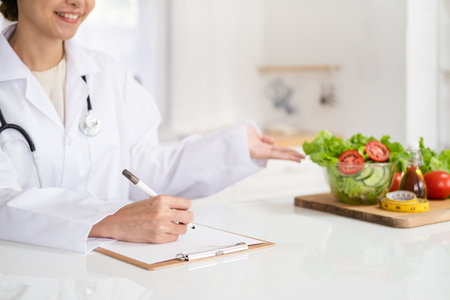 Woman dietitian in medical uniform with stethoscope working on a diet plan sitting with different healthy food ingredients in  office on background. Weight loss and right nutrition conceptの写真素材