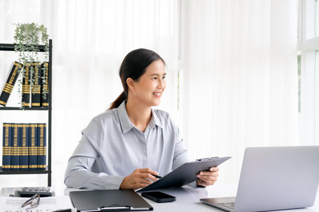 Successful smiling mature businesswoman using laptop and computer while doing some paperwork at the office.の写真素材