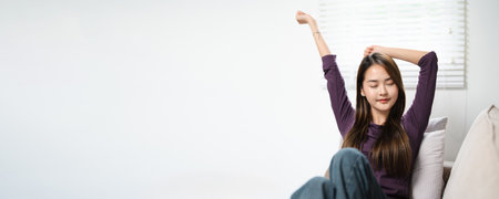 Well rested woman lying on soft cushions stretching body muscles raises her arms on cozy sofa after...