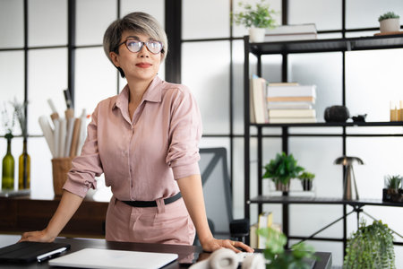 Mature asian business woman smiling looking away confident at home office. Happy  woman professional posing in modern creative office space.の写真素材