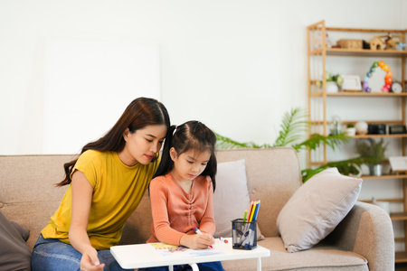Asian moms are teaching crayon skills to Daughters. To draw a line. Write book on paper Artistic development Imagine And the mood of the children very well. And the family is very understanding love.の写真素材