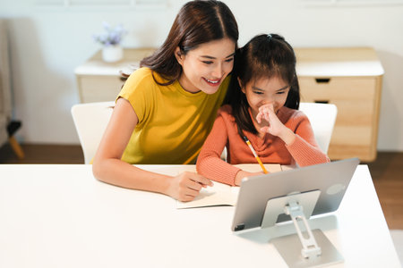 Loving young mum and little preschooler daughter sit at table using laptop tablet together, caring mother help small girl child teaching learning online on computer, kids and technology conceptの写真素材