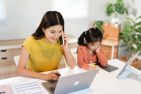 pretty young woman works from home doing home office and her daughter has homeschoolingの写真素材