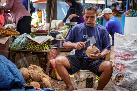 old man opening coconut with axe in traditional marketのeditorial素材