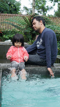 young father with a beard was playing water with his little girl in the poolのeditorial素材