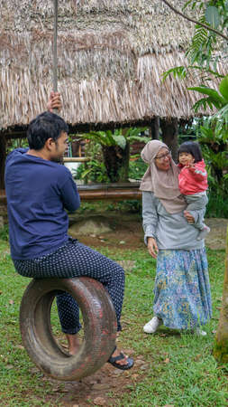 BOGOR, INDONESIA - 16 December 2018 : Happy Muslim family is playing swing from the tire togetherのeditorial素材