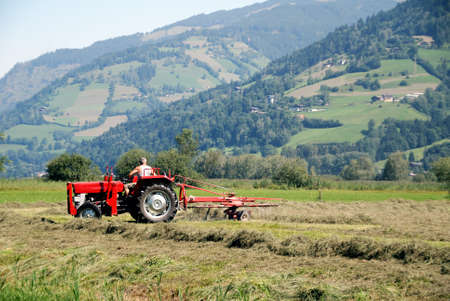Tractor plowing in front of mountains in austrian farmの写真素材