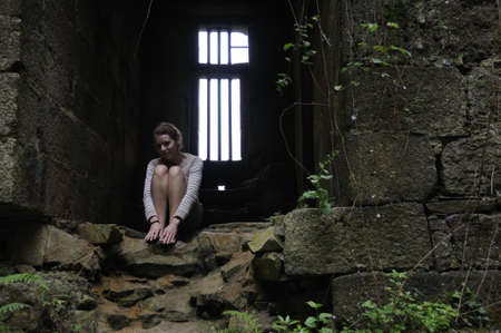 Young woman sitting in dungeon of old castle in Brittanyの写真素材