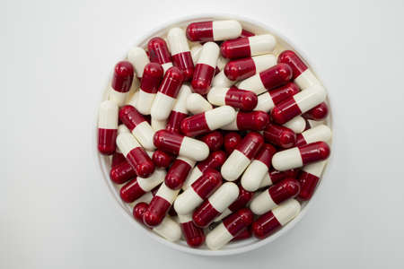 Top view of red, white, capsule pills in plastic container on white backgroundの写真素材