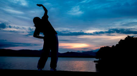 The silhouette of a woman exercising on the edge of a reservoir behind the mountainの写真素材