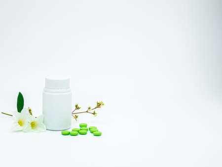 Green vitamin and supplement tablet pills with flower and branch and blank label plastic bottle on white background with copy space, just add your own textの写真素材