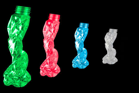 Green, red, blue and white twisted plastic bottles are shaped like four people walking in a row on black background with copy spaceの写真素材
