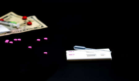 Two methamphetamine cassette test and plastic dropper with pink drugs, american dollar bills and syringe as blur dark background with copy spaceの写真素材