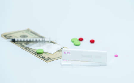 Two methamphetamine cassette test and plastic dropper with red, pink and green drugs, fake heroin powders, american dollar bills and syringe and needle on white background with copy spaceの写真素材
