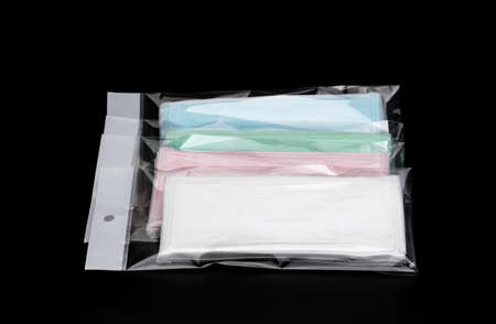 Green, pink, light blue and white ear loop disposable face mask in plastic bag overlapping, used for covering mouth and nose. It protects against body fluid and large particles in the airの写真素材