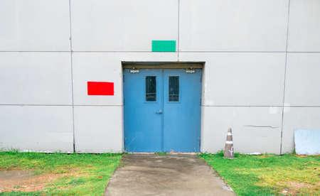 Closed blue door with green and red text box on white concrete wall, grass and walkway with copy spaceの写真素材